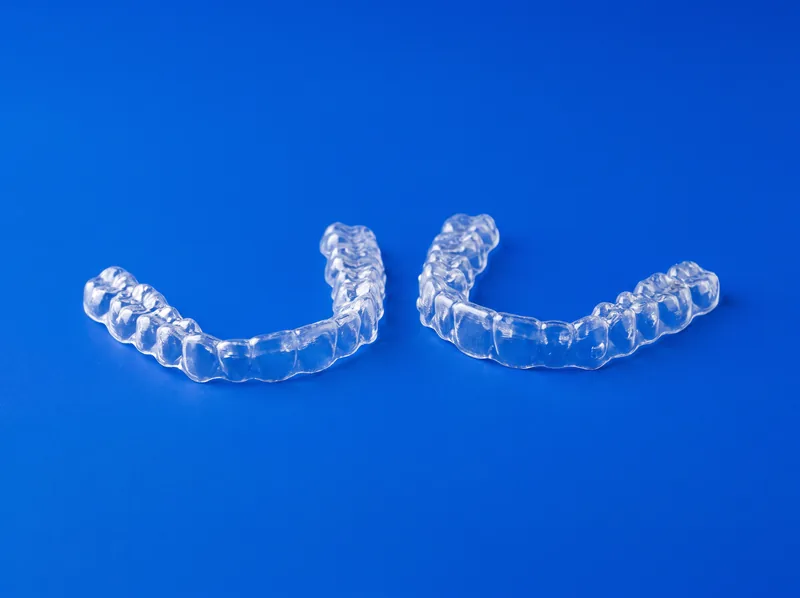 Zwei transparente Aligner für Ober- und Unterkiefer vor kobaltblauem Hintergrund